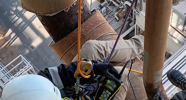 Technician performing ultrasonic thickness inspection (UT) on industrial pipes using rope access techniques