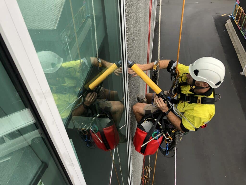 Technician performing rope access expansion joint replacement on a high-rise building, wearing safety gear and working efficiently on the exterior facade