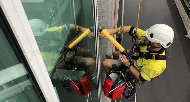 Technician performing rope access expansion joint replacement on a high-rise building, wearing safety gear and working efficiently on the exterior facade