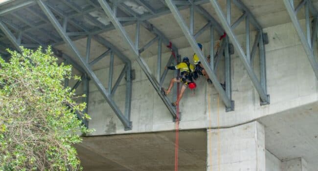 Industrial abseilers from Connect Access performing rope access inspection and maintenance work under a concrete bridge structure.