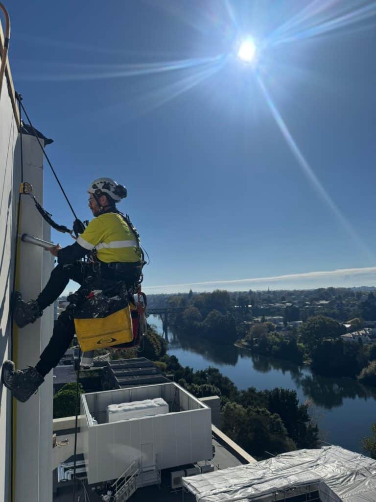 An IRATA-certified rope access technician working on a commercial building exterior.