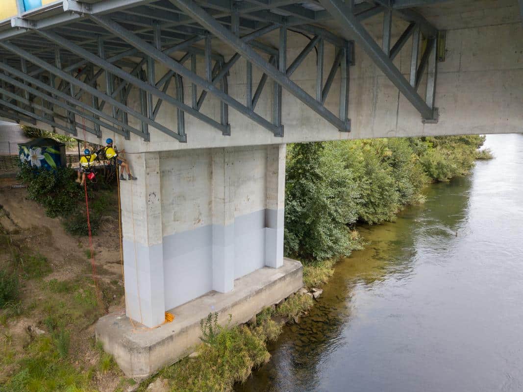 Connect Access rope access technicians working on a concrete bridge pillar over a river.