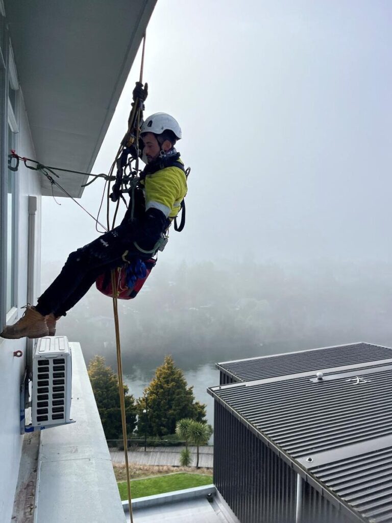 An IRATA-certified rope access technician cleaning high-rise windows on a dual-rope system.