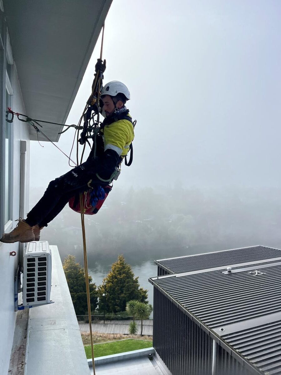 An IRATA-certified rope access technician cleaning high-rise windows on a dual-rope system.