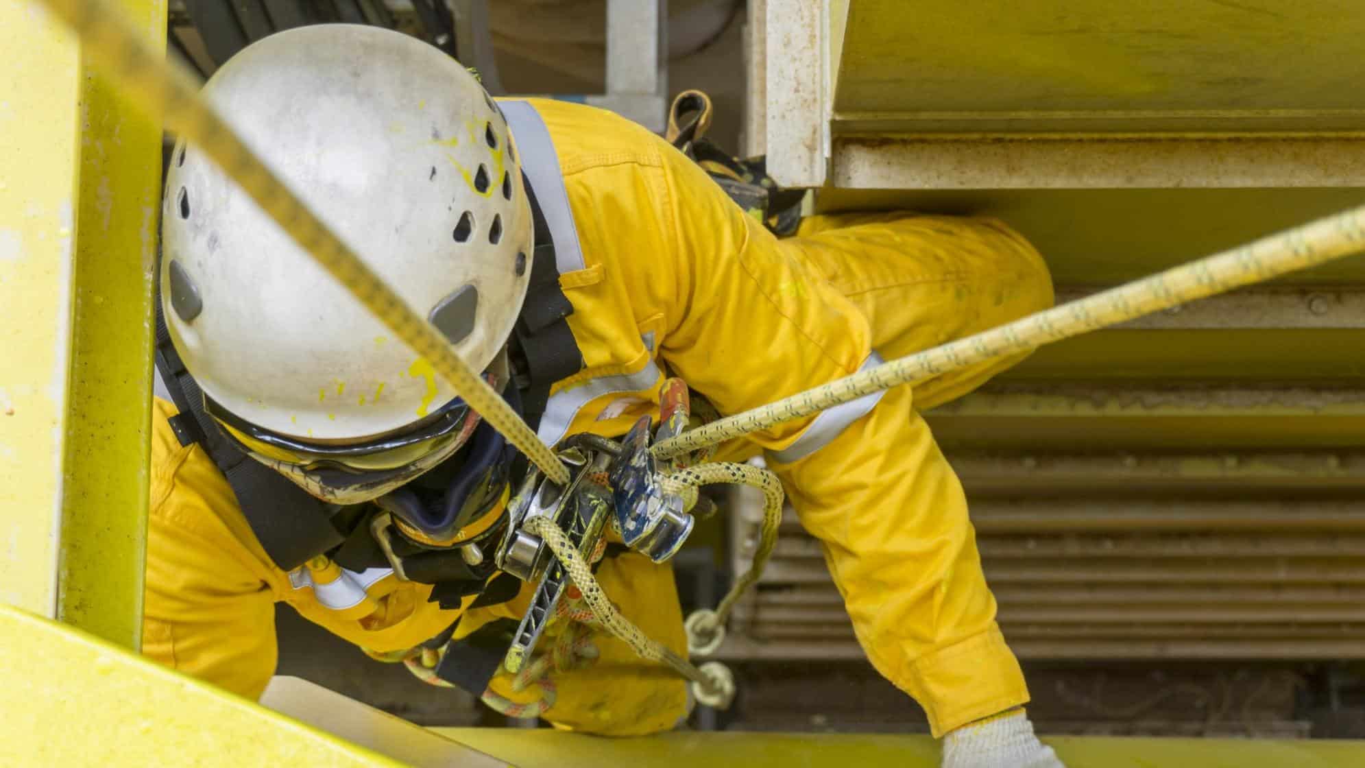 abseiler with a hard hat hangs from a secure harness and rope